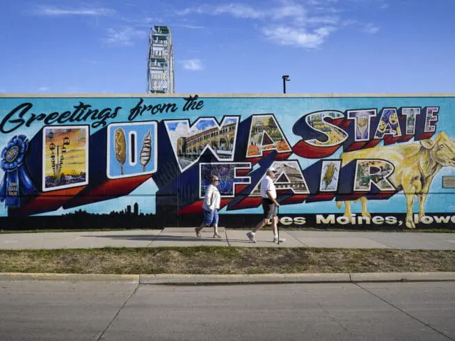 Fairgoers walk past a mural at the Iowa State Fair, Friday, Aug. 19, 2022, in Des Moines, Iowa.